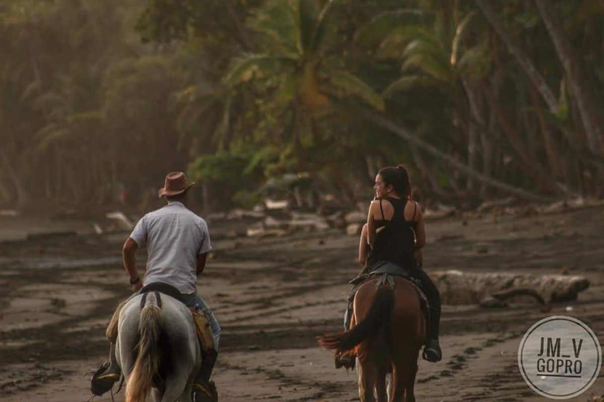 Two riders on horseback along the beach at sunset near Pavones