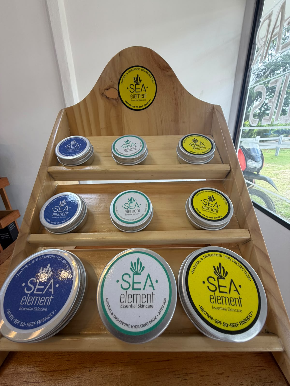 Sea Element reef-friendly SPF 50 sunscreen and after-sun balm tins on a wooden display stand in the shop