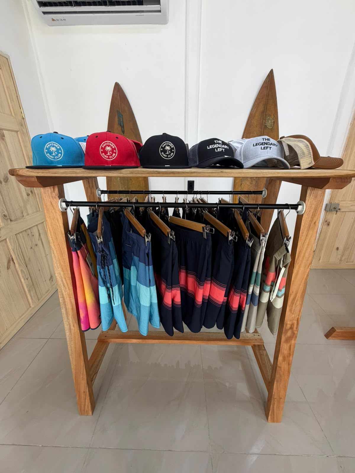 Pavones Surf Club caps and Billabong boardshorts on a handmade wooden rack inside the surf shop in Pavones, Costa Rica